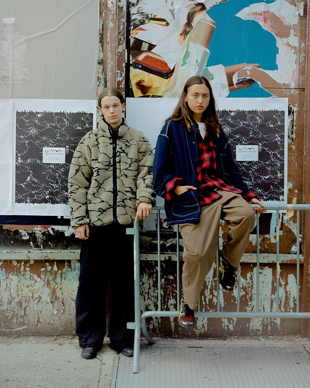 One male, one female model pose in front of wall wearing AW23 Manastash